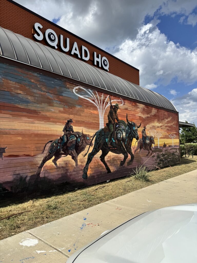 Squad HQ mural by Utsav Adhikari — cowboys riding robotic bulls across a sunset, painted on a Texas commercial building